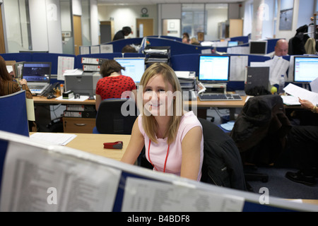 Une jeune fille s'arrête ses fonctions assise à son bureau avec des collègues de travail à l'œuvre dans l'arrière-plan d'un open plan office Banque D'Images