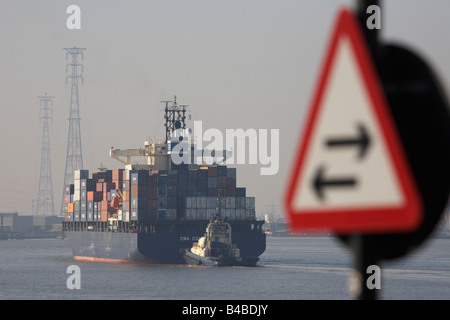 Passé un signe, un cargo porte-conteneurs géant est guidée par un remorqueur, l'assouplissement en amont sur la Tamise vers Tilbury Docks Banque D'Images