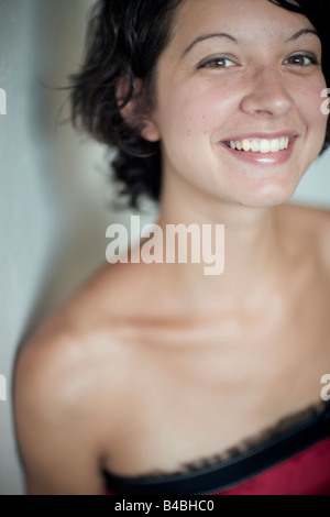 Tête de jeune femme aux cheveux noirs portant une robe rouge sans bretelles mignon regardant la caméra et smiling Banque D'Images