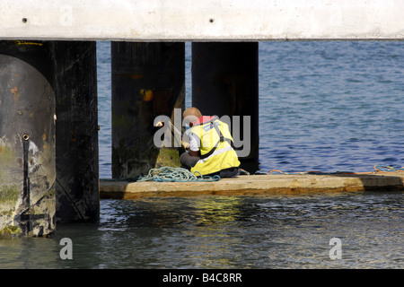 Workman assis sur un petit radeau à l'aide d'un chalumeau à gaz pour couper et souder une jambe jetée en acier Banque D'Images