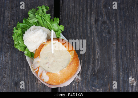 Pain au levain bol rempli de clam chowder sur un quai rambarde en face d'une canne à pêche Banque D'Images