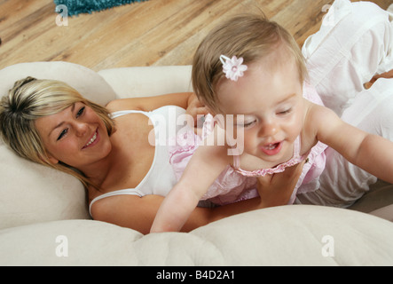 Jeune mère couchée sur un canapé avec sa petite fille de 9 mois, pouvant atteindre jusqu'à commandes Banque D'Images