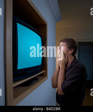 Un homme d'âge moyen est très près de la télévision et regarder mais à la choqué et horrifié un chemin pour l'écran est inclus. Banque D'Images