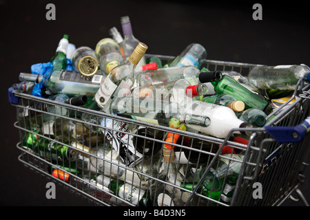 Un chariot de supermarché plein de bouteilles et canettes de boissons vides en attente de collection sur le trottoir devant une télévision à Birmingham. Banque D'Images
