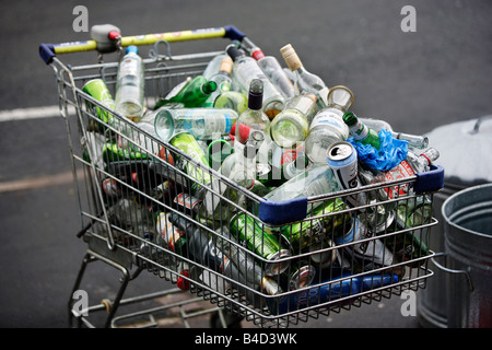 Un chariot de supermarché plein de bouteilles et canettes de boissons vides sur le trottoir devant une télévision à Birmingham. Banque D'Images