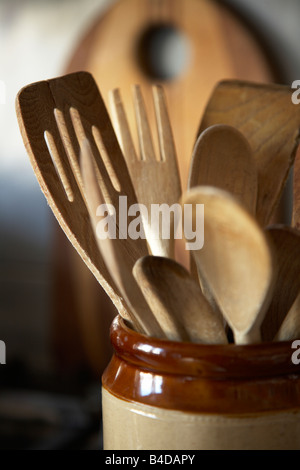 Ustensiles de cuisine en bois brun dans un pot avec une planche derrière dans la cuisine cuisine Banque D'Images