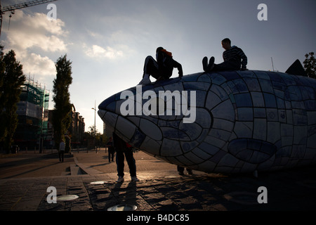 Les enfants jouent sur le gros poisson sculpture du saumon par John gentillesse à côté de la rivière Lagan dans Belfast City Centre Banque D'Images