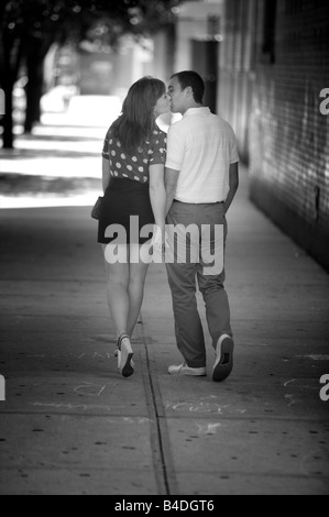 Jeune couple amoureux voler un baiser comme ils flâner le long d'une avenue de New York. Ou est-ce Paris ? Rome ? Adorable, cette période de l'année. Banque D'Images