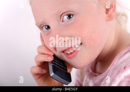 Tête et épaule rapprochée sur une petite blonde aux cheveux bruns, blue-eyed girl talking on a mobile/téléphone cellulaire et souriant. Banque D'Images