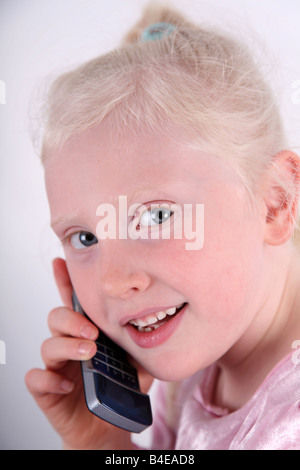 Tête et épaule rapprochée sur une petite blonde aux cheveux bruns, blue-eyed girl talking on a mobile/téléphone cellulaire et souriant. Banque D'Images