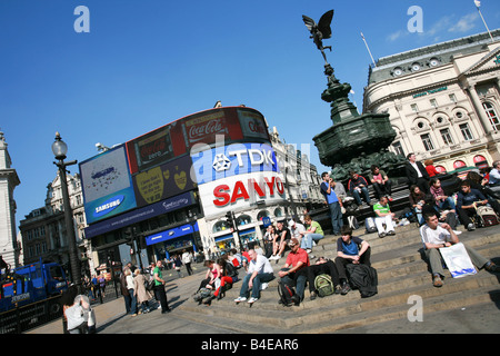 Les touristes reste sur mesures en vertu de l'Eros statue fontaine de Piccadilly Circus avec de célèbres enseignes publicitaire néon derrière l'angle inhabituel Banque D'Images