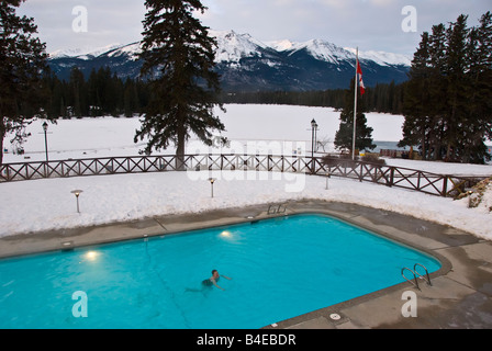 Femme seule la natation dans une piscine extérieure avec de la neige et des montagnes en arrière-plan, le Jasper Park Lodge, Canada Banque D'Images