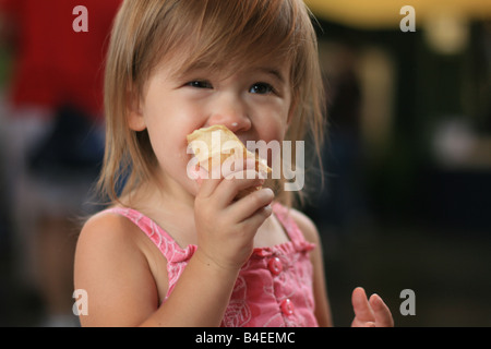 Un 2-year-old girl mange un cornet de crème glacée. Banque D'Images