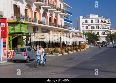 L'homme sur Motor Scooter passé Hôtel et Taverne sur bord de mer de la ville de Tinos Île de Tinos Cyclades Grèce Banque D'Images