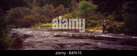 Une vue panoramique vue d'un homme qui pourrait être un braconnier ou un jeu keeper debout dans un ruisseau qui coule en Ecosse fly fishing Banque D'Images