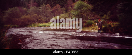 Une vue panoramique vue d'un homme qui pourrait être un braconnier ou un jeu keeper debout dans un ruisseau qui coule en Ecosse fly fishing Banque D'Images