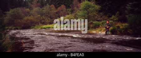 Une vue panoramique vue d'un homme qui pourrait être un braconnier ou un jeu keeper debout dans un ruisseau qui coule en Ecosse fly fishing Banque D'Images