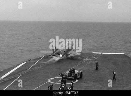 L'équipage de pont à bord du HMS Ark Royal protéger leurs oreilles comme un fantôme de McDonnell Douglas FG1 F 4K de 892 Sqd FAA tonnerres au loin avec postcombustion complet au décollage Banque D'Images