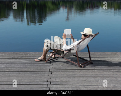 Un jeune homme assis dans une chaise longue sur une jetée de lire un livre Banque D'Images