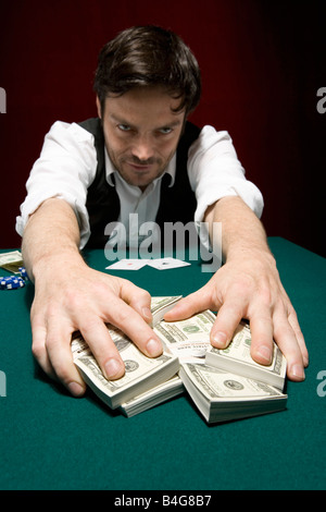 Un homme à une partie de poker High Stakes tirant une pile d'argent vers lui Banque D'Images