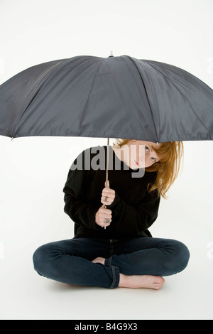 Une jeune femme assise jambes croisées sous un parapluie Banque D'Images