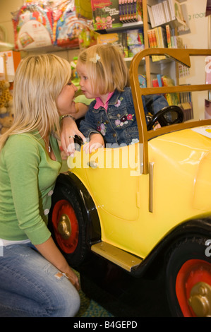 Petite fille et sa mère jouant avec un grand jouet voiture dans un magasin de jouets Banque D'Images