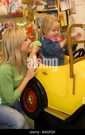 Petite fille et sa mère jouant avec un grand jouet voiture dans un magasin de jouets Banque D'Images