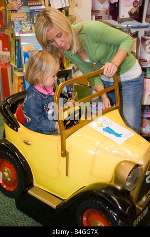 Petite fille et sa mère jouant avec un grand jouet voiture dans un magasin de jouets Banque D'Images