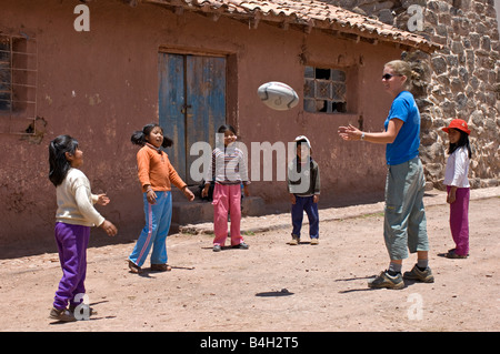 Une femme visite du village touristique se fait des amis avec les enfants en jouant 'rugby' avec eux. Banque D'Images