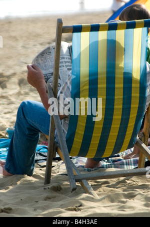 Homme assis dans une chaise longue sur la plage de Bournemouth reading a newspaper Banque D'Images