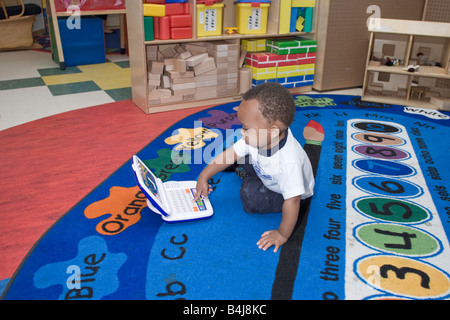 Préscolaire afro-américaine garçon assis sur le sol à jouer avec un jouet portable, Banque D'Images