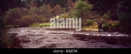 Une vue panoramique vue d'un homme qui pourrait être un braconnier ou un jeu keeper debout dans un ruisseau qui coule en Ecosse fly fishing Banque D'Images