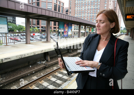 La navette businesswoman maintient occupé en attendant l'arrivée de son train Banque D'Images