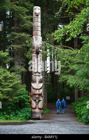 Les visiteurs passer le gros totem à l'entrée du sentier dans le parc historique national de Sitka Sitka en Alaska Banque D'Images