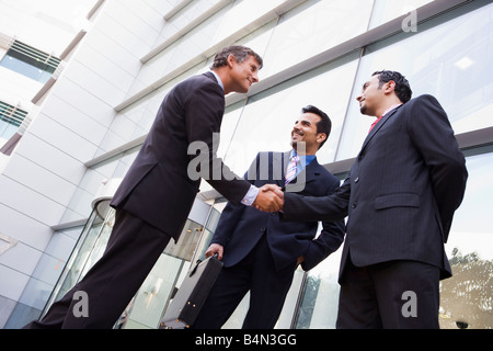 Trois hommes d'affaires de bâtiment shaking hands and smiling (high key/focus sélectif) Banque D'Images