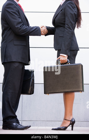 Two businesspeople standing outdoors holding porte-documents et shaking hands Banque D'Images