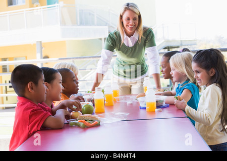 Enseignant en s'appuyant sur le tableau à l'extérieur, tandis que les étudiants prennent leur repas de midi (high key) Banque D'Images