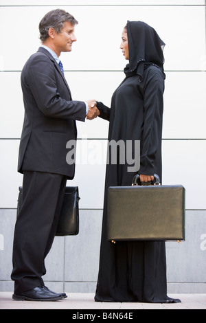 Two businesspeople shaking hands and smiling outdoors Banque D'Images