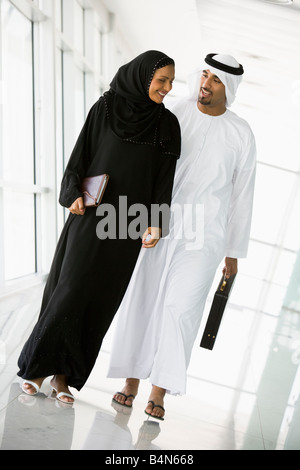 Deux businesspeople walking in corridor smiling (high key/focus sélectif) Banque D'Images