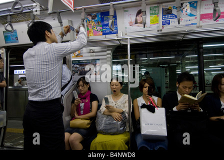 Les usagers du métro de Tokyo sur l'oeil à leurs téléphones portables et de lire. Usagers dans le métro de Tokyo avec leur téléphone portable. Banque D'Images