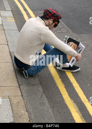 Un jeune homme à la mode se trouve sur le trottoir de la lecture d'un magazine de mode à Middlesbrough England UK Banque D'Images