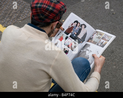 Un jeune homme à la mode se trouve sur le trottoir de la lecture d'un magazine de mode à Middlesbrough England UK Banque D'Images