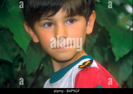 Portrait d'un petit garçon à la recherche d'un papillon à assis sur son épaule Banque D'Images