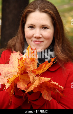 Portrait d'une belle jeune femme tenant les feuilles d'automne dans les mains sur un fond de feuilles en automne. Banque D'Images