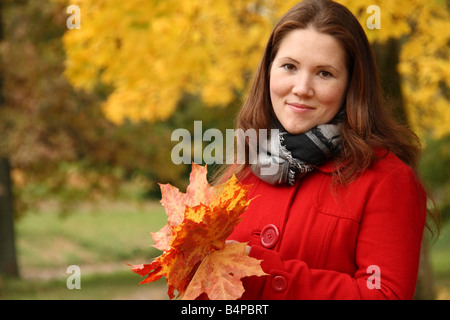 Portrait d'une belle jeune femme tenant les feuilles d'automne dans les mains sur un fond de feuilles en automne. Banque D'Images