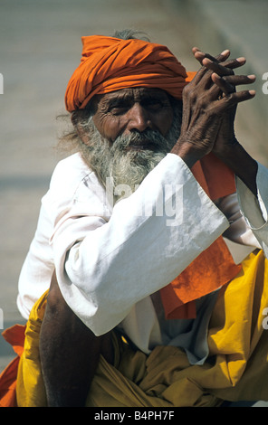 Les mains jointes, Indien homme portant un turban orange, chemise de coton blanc et jaune dhoti reposant sur ghat de Varanasi, Inde Banque D'Images