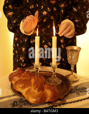 Femme avec un match des bougies d'éclairage, et des symboles du Shabbat sur la table y compris la challah et kiddish cup Banque D'Images