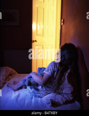 Fille dans sa chambre de câliner un ours, la porte est ouverte avec la lumière en streaming. Banque D'Images