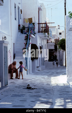 Petit garçon parle à l'homme dans une ruelle blanchis à la cat avec chaise longue sur l'île de Mykonos, Grèce, Europe Banque D'Images