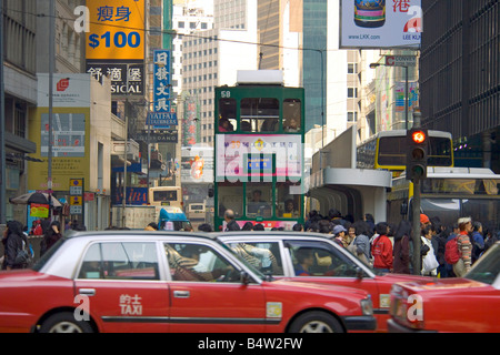 Un tramway traditionnel vieux qui voyagent à travers la zone Wan Chai de Hong Kong Island avec le taxi rouge au premier plan. Banque D'Images